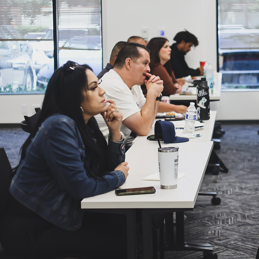 Engaged Adults Learning in a Professional Classroom Setting Diverse group of adults attending a class or seminar, focused on a speaker, with notebooks and drinks on tables.