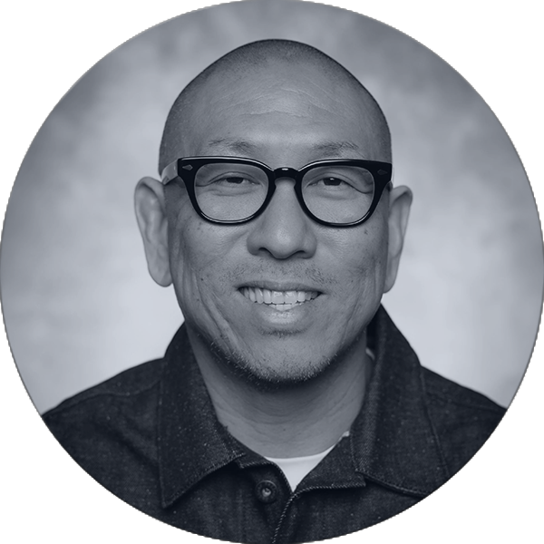 Executive Team Member Professional Headshot Bald East Asian man with black glasses and stubble smiles warmly in a grayscale headshot.
