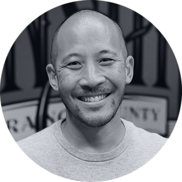 Smiling Executive Team Member Portrait Smiling man, bald with a short beard, wearing a grey sweater in a black and white circular portrait.