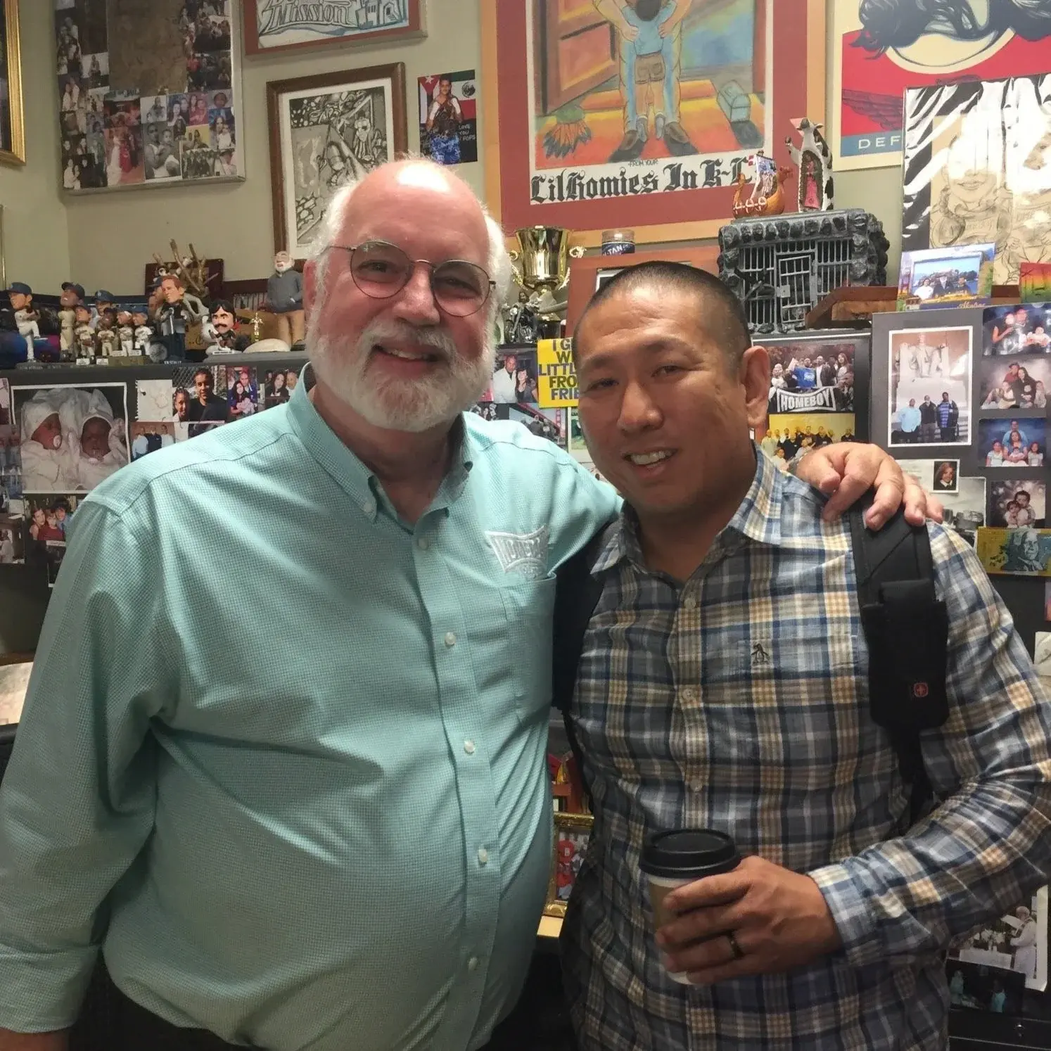 Founders and Friends: Our Story Connection Two men, one older with a white beard and glasses, and one younger Asian man, smiling together in a memorabilia-filled room.