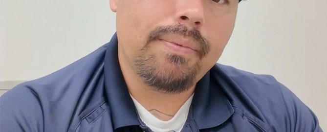 A man with a goatee and mustache, wearing a navy blue 'Project Kinship' baseball cap and polo shirt, looking directly at the…