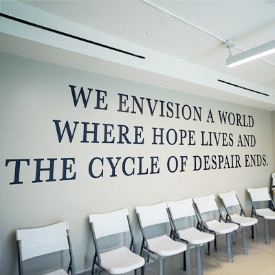 Kinship Heals: Envisioning Hope, Ending Despair Motivational wall text 'WE ENVISION A WORLD WHERE HOPE LIVES AND THE CYCLE OF DESPAIR ENDS' in a room with white chairs.