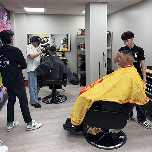 Hands-On Barber Training for Workforce Development Barber students practice haircuts on clients in a modern training facility, observed by an instructor, demonstrating hands-o…
